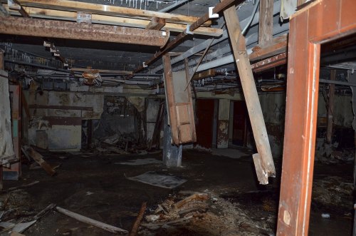 An abandoned, dilapidated room with exposed beams, debris, and peeling walls, creating a haunting atmosphere.