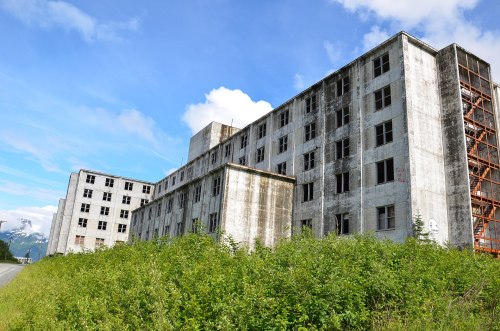 Abandoned concrete buildings surrounded by overgrown greenery under a blue sky with scattered clouds.