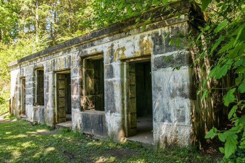 Abandoned stone structure surrounded by greenery, featuring multiple doorways and weathered walls.