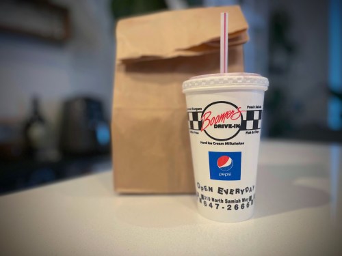 A milkshake cup from Boomer's Drive-In next to a brown paper bag on a countertop.