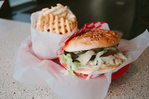 A sesame seed bun burger with lettuce and pickles, served with a side of waffle fries in a red-checkered basket.