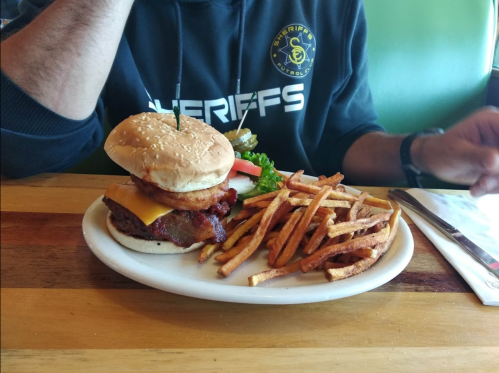 A cheeseburger with bacon, lettuce, and tomato, served with a side of sweet potato fries on a plate.