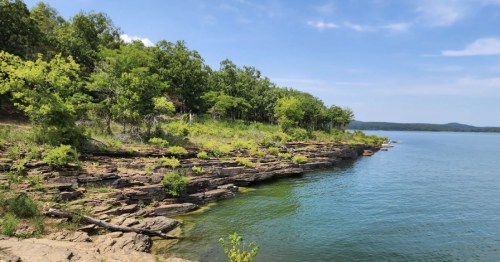 A serene lakeside view with rocky shorelines and lush green trees under a clear blue sky.