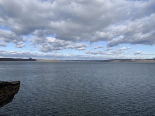 A serene view of a calm lake surrounded by hills under a cloudy sky.