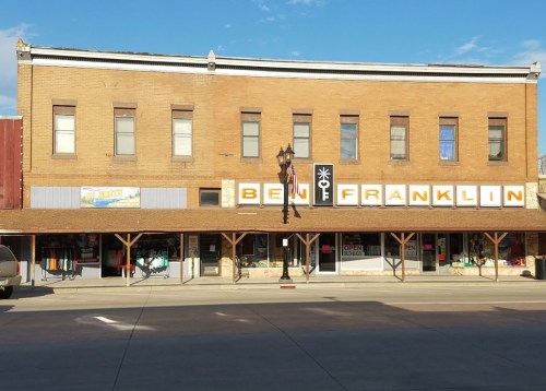 Historic brick building with shops, featuring a large "Ben Franklin" sign and a clear blue sky above.