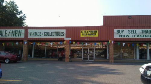 Exterior of a flea market with banners for vintage items and leasing, colorful flags, and parked cars in front.