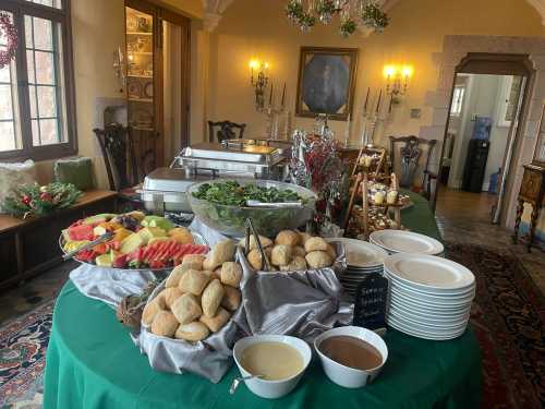 A festive buffet table with salads, fruits, rolls, and sauces, set in a warmly decorated dining room.