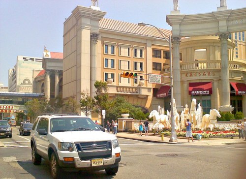 A white SUV parked near Caesars Palace, featuring grand architecture and a fountain with horse sculptures.
