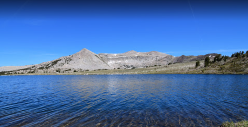 A serene lake reflects a clear blue sky, surrounded by mountains and grassy terrain.