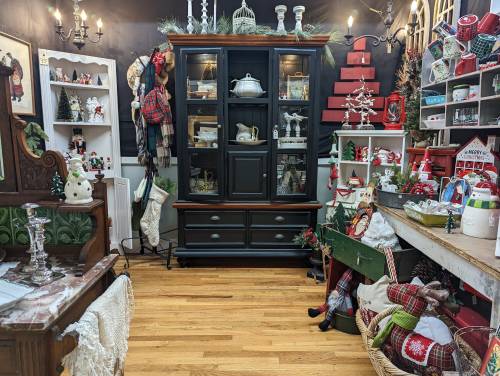A cozy holiday-themed shop with festive decorations, a black cabinet, and various seasonal items displayed on shelves.