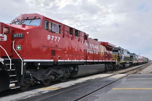 A red Canadian Pacific locomotive parked on a railway track, with additional train cars visible in the background.
