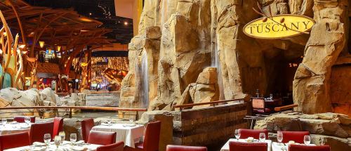 Interior of a restaurant with rock formations, water features, and red chairs at elegantly set tables.