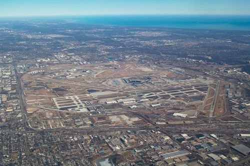 Aerial view of a large airport with runways, taxiways, and surrounding urban areas near a body of water.