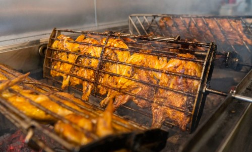Rotating skewers of grilled chicken and wings cooking over an open flame in a restaurant kitchen.