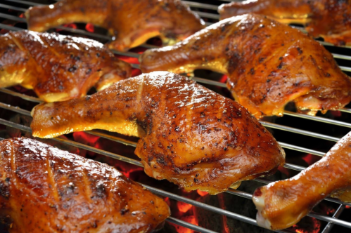 Grilled chicken legs sizzling on a barbecue grill, glistening with marinade and smoke.
