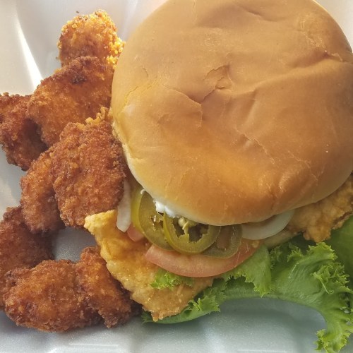A plate featuring a crispy chicken sandwich with lettuce, pickles, and a side of golden fried chicken tenders.