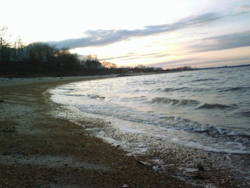 A serene beach at sunset, with gentle waves lapping at the shore and a cloudy sky in the background.