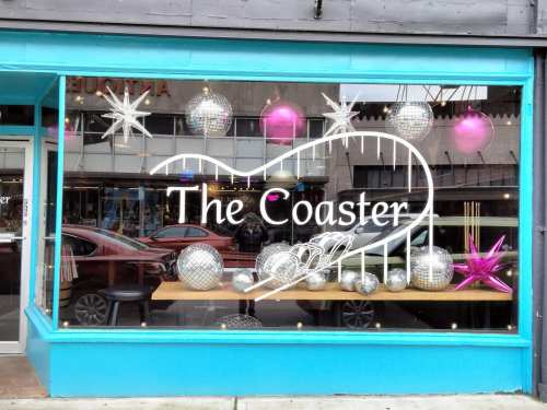Storefront window display featuring festive decorations, including silver and pink ornaments, with "The Coaster" sign.