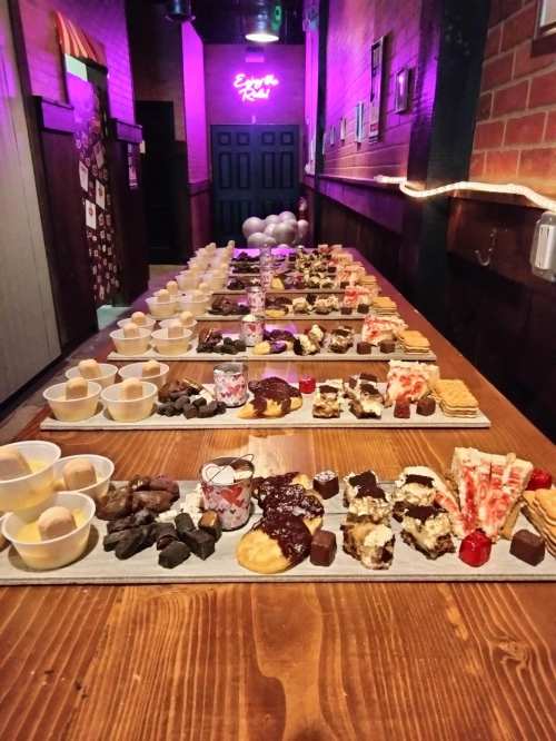 A long table filled with various desserts, including cakes, chocolates, and pastries, under colorful lighting.