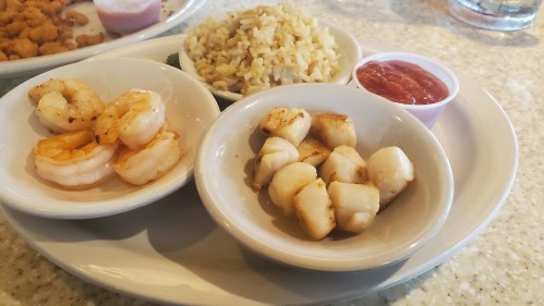 A plate with grilled shrimp, scallops, fried rice, and a small cup of dipping sauce.