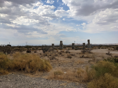 Desert landscape with stone ruins and sparse vegetation under a cloudy sky.