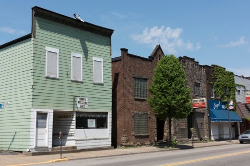 A row of buildings featuring a green structure, brick facades, and a tree, under a clear blue sky.