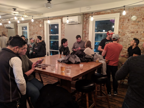 A lively gathering in a rustic bar with people chatting, drinking, and enjoying each other's company around a large table.