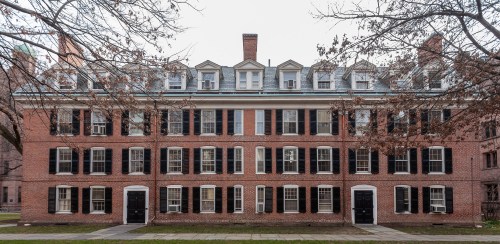 A historic brick building with multiple windows and black shutters, surrounded by bare trees.