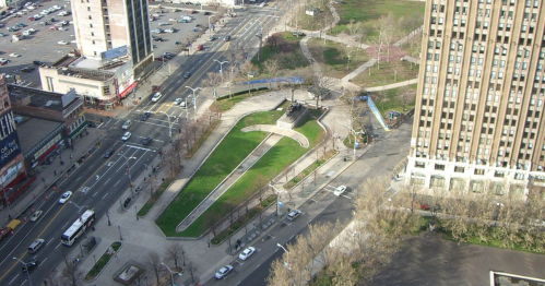 Aerial view of a park with pathways and greenery, surrounded by city streets and buildings.
