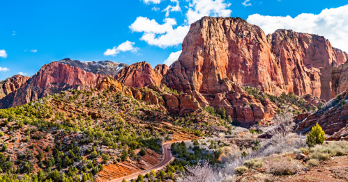 A scenic view of red rock formations and green vegetation under a blue sky with scattered clouds.