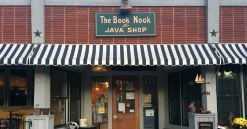Exterior of The Book Nook & Java Shop, featuring a striped awning and wooden door, with a cozy, inviting atmosphere.