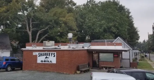 A brick building with a sign reading "Sharkey's Grill," surrounded by trees and parked cars.