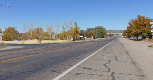 A wide, empty road lined with trees in autumn colors under a clear blue sky.