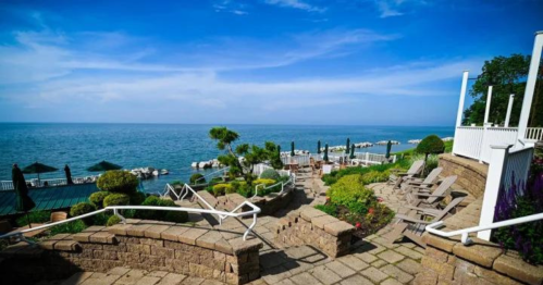 Scenic view of a lakeside patio with chairs, greenery, and umbrellas under a clear blue sky.