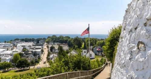 A scenic view of a coastal town with a flag, trees, and a pathway leading down to the water.