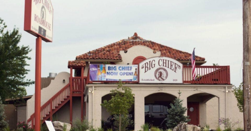 A building with a sign reading "Big Chief" and a banner announcing its opening, surrounded by trees and landscaping.