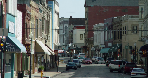 A quaint downtown street lined with historic buildings, shops, and parked cars under a clear blue sky.