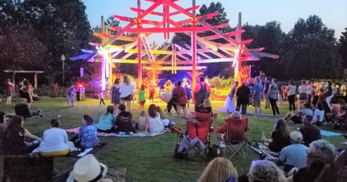 A lively outdoor event with a crowd gathered around a colorful stage, enjoying music and performances at dusk.