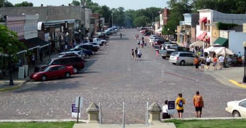 The historic main street in Cottonwood Falls, KS, lined with cars and pedestrians on a sunny day.