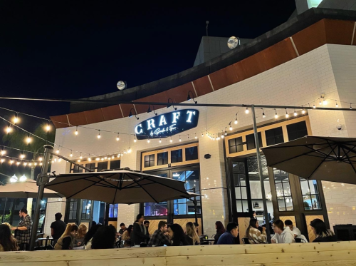 A lively outdoor dining area at night, featuring string lights and a sign that reads "CRAFT." People are seated at tables.