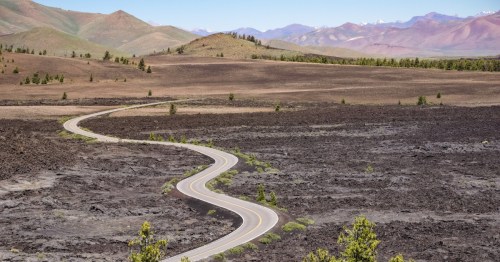 A two-lane road winds through a hardened lava field within Idaho's Craters of the Moon National Monument and Preserve.