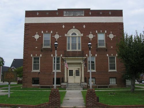 A brick building with decorative elements, featuring a central entrance and two American flags, surrounded by grass.