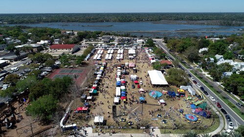 Aerial view of a lively outdoor festival with tents, activities, and a river in the background.