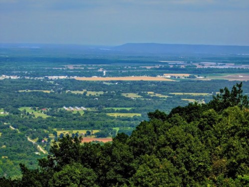 A panoramic view of lush green fields and distant hills under a clear blue sky.
