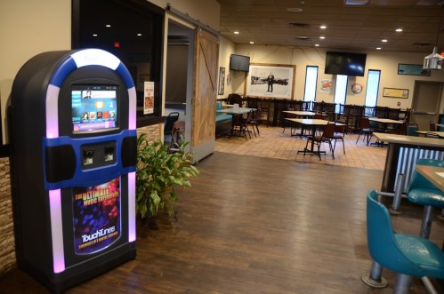 A jukebox stands in a casual dining area with empty tables and a warm, inviting atmosphere.