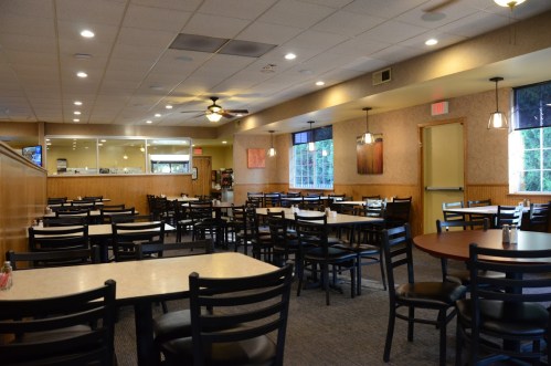 A spacious, empty restaurant with tables and chairs, warm lighting, and a counter in the background.