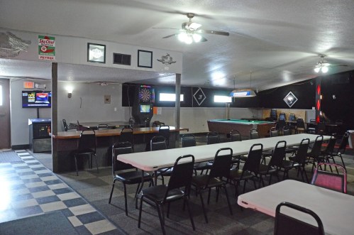 Interior of a casual bar with pool table, dartboard, and rows of empty tables and chairs.
