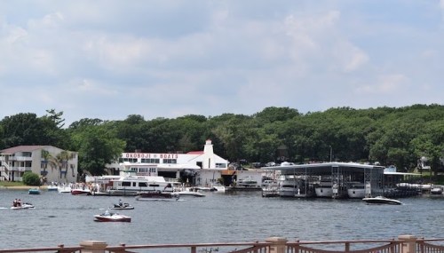 A scenic view of a marina with boats on the water and a restaurant in the background, surrounded by greenery.