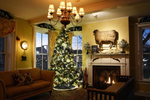 Cozy living room with a Christmas tree, fireplace, and a decorative cow statue on the wall, warmly lit at dusk.
