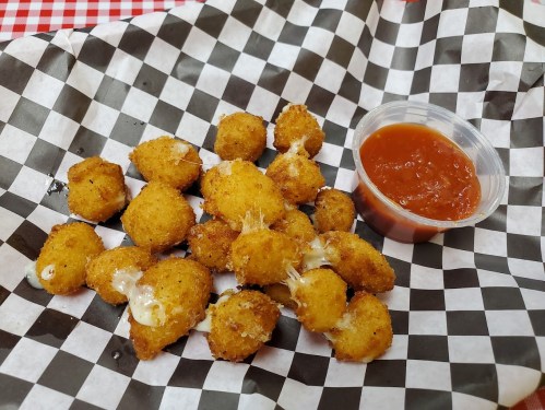 A plate of golden, crispy cheese bites served with a side of marinara sauce on a checkered paper.